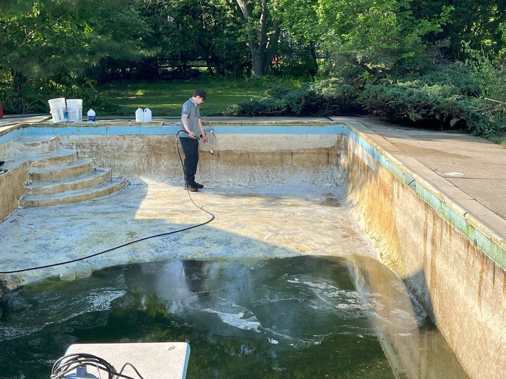 Drained backyard pool with a man standing inside, green trees and patio surrounding it