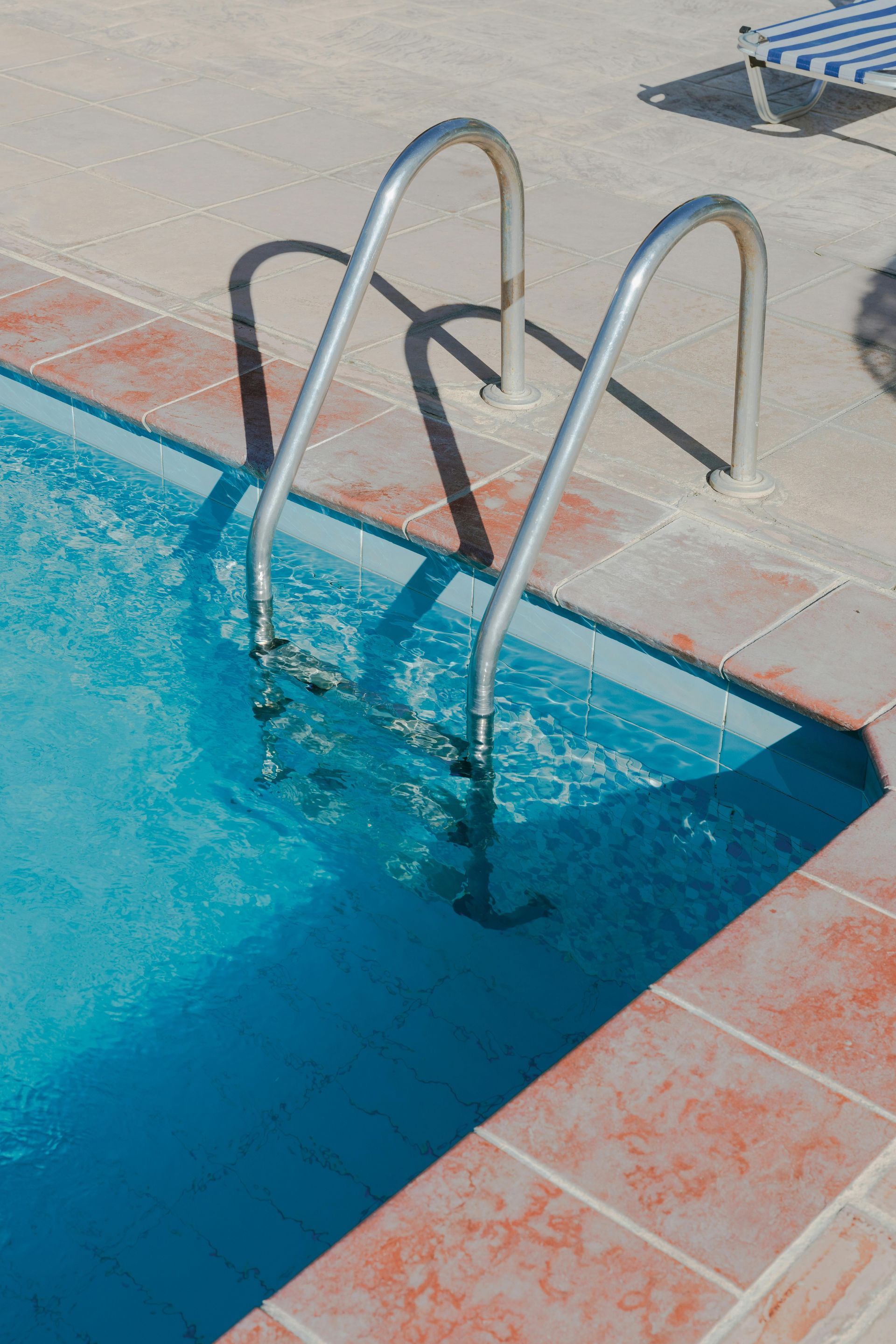 Pool ladder beside a blue swimming pool with red-tiled deck