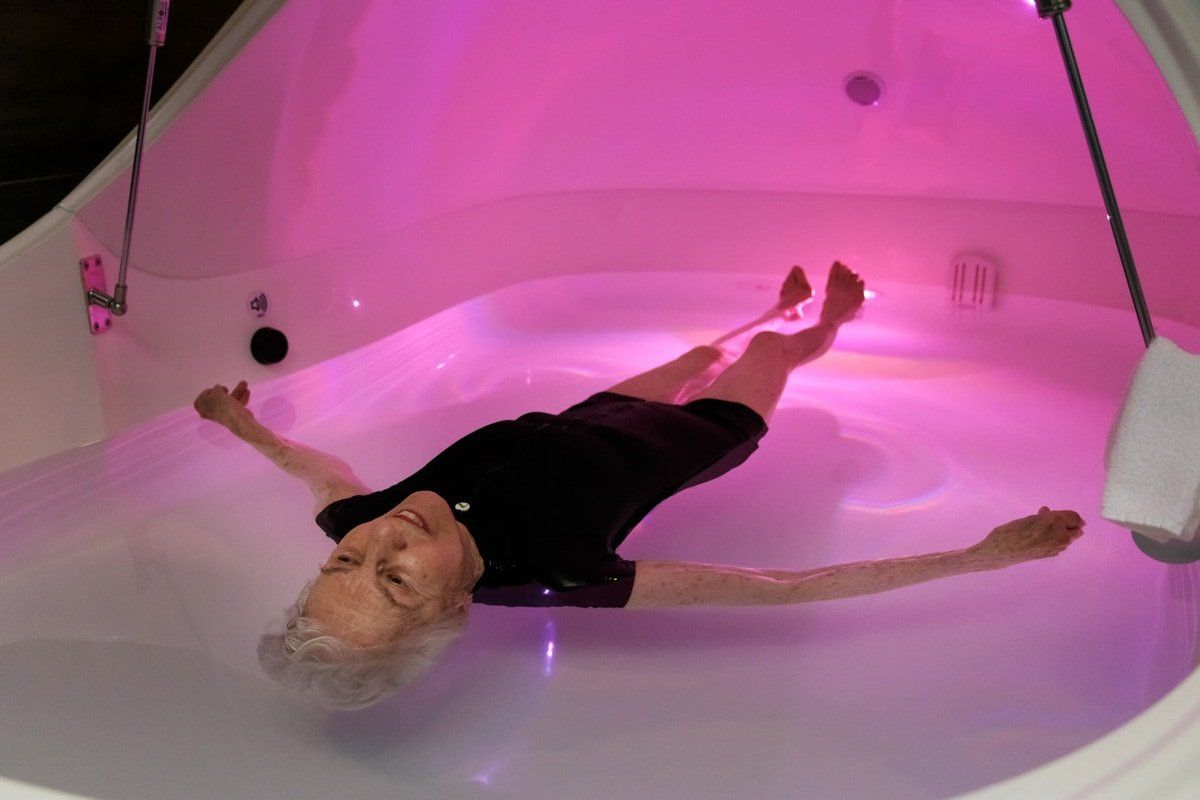 A woman is floating in a pink bathtub.