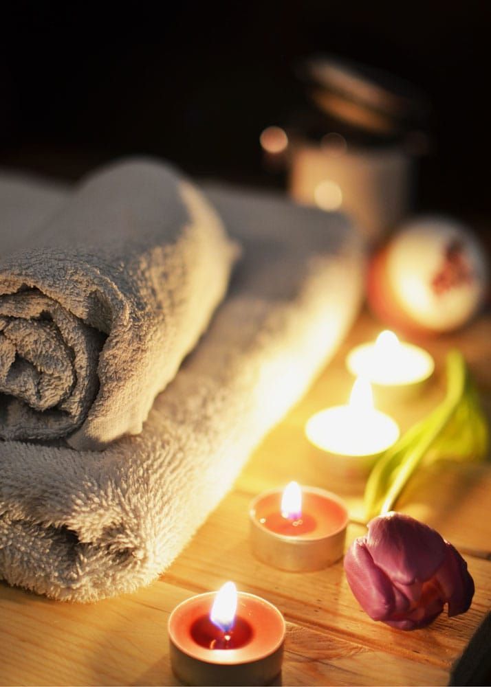 A stack of towels sitting on top of a wooden table next to candles and a flower.