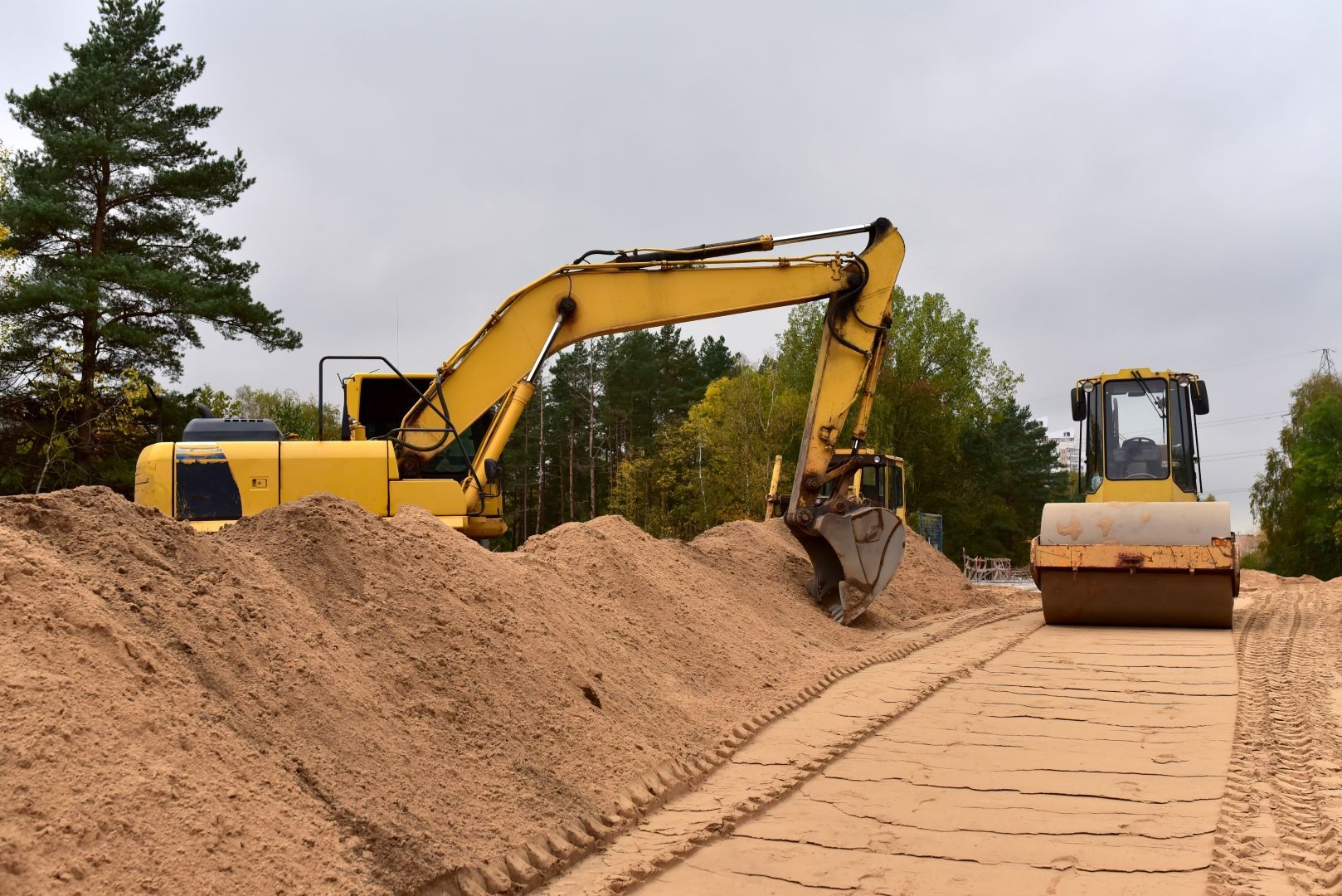 Excavator Loading Sand Beside a Road Roller — A & S Cuthel Earthmoving & Transport in Nambucca Heads, NSW