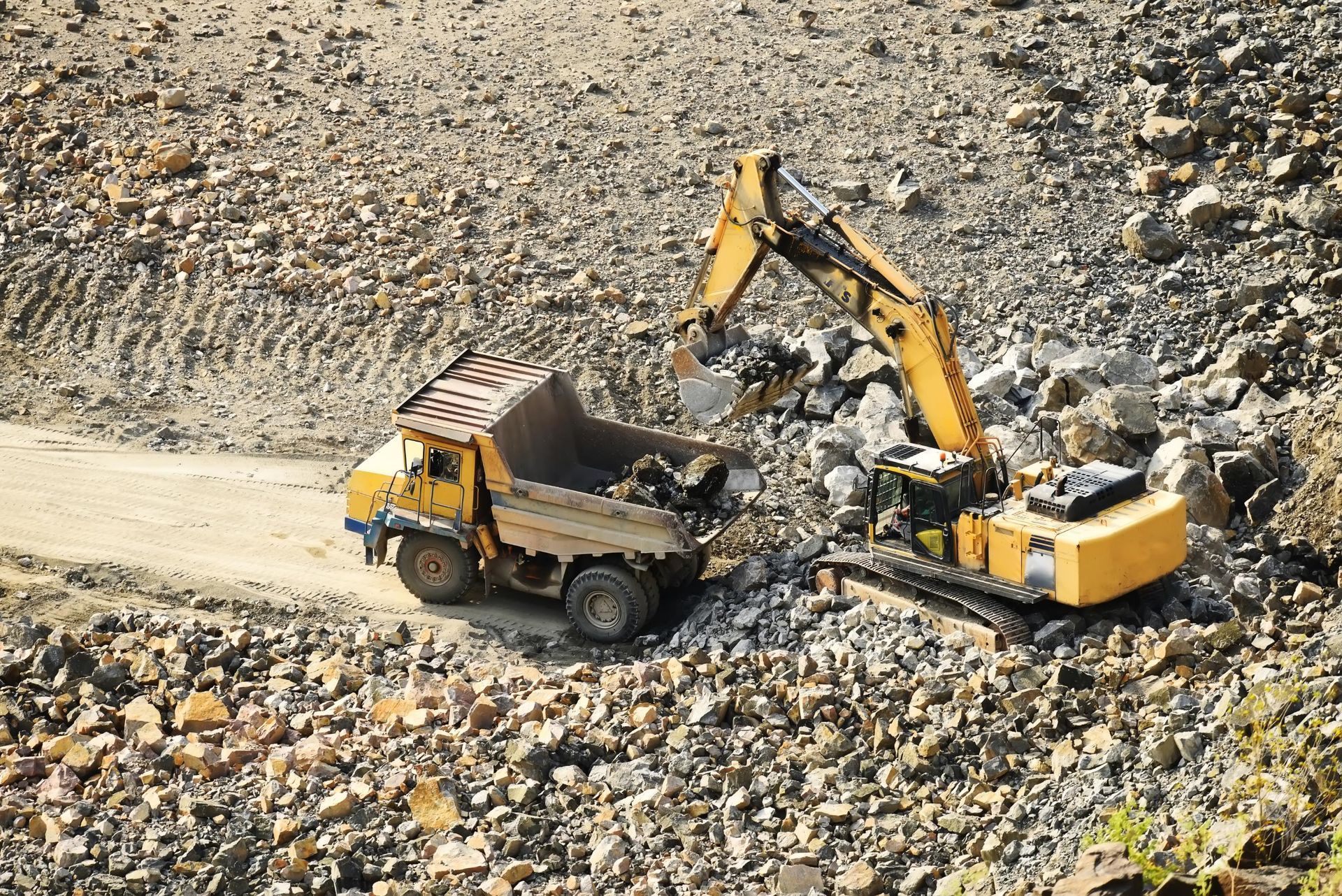 Yellow Excavator and Dump Truck Loading Rocks at A Quarry Site — A & S Cuthel Earthmoving & Transport in Coffs Harbour, NSW