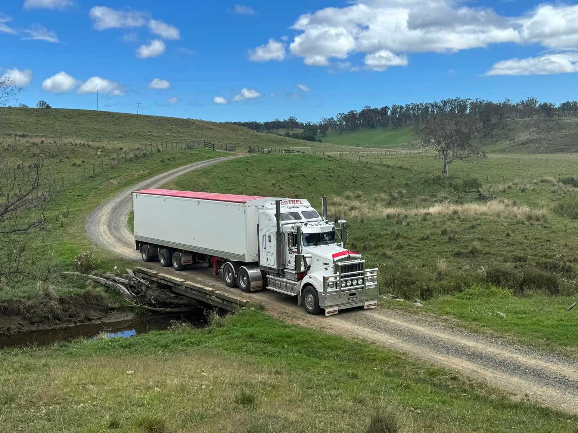 White Semi Truck Driving on A Dirt Road Through Green Hills — A & S Cuthel Earthmoving & Transport in Bellingen, NSW