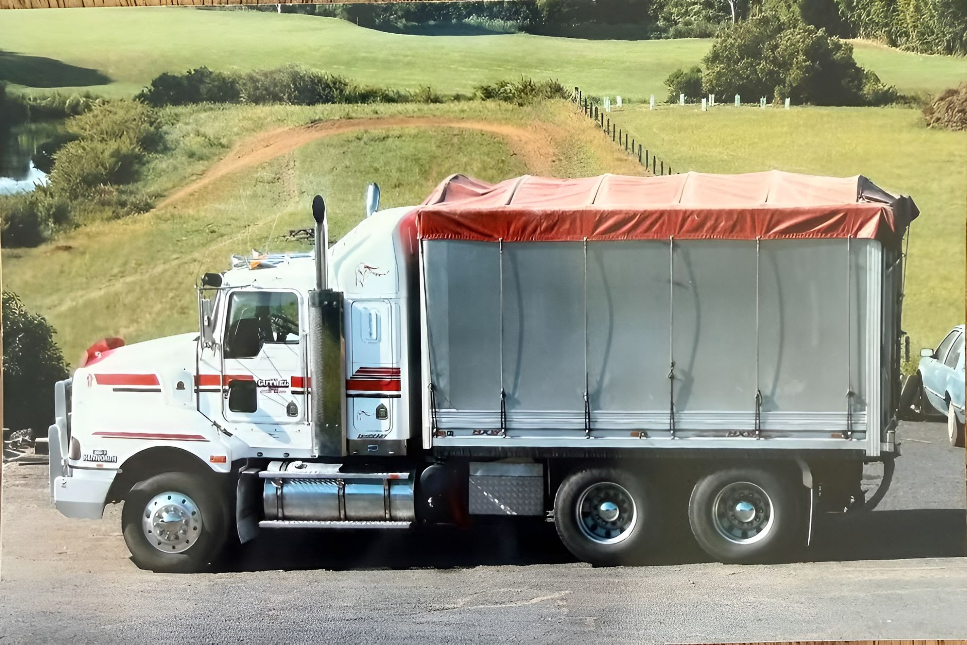 White Dump Truck with Red Tarp Parked on A Rural Road Beside Green Fields — A & S Cuthel Earthmoving & Transport in Nambucca Heads, NSW