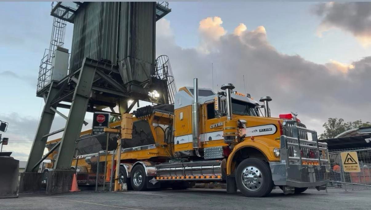 Yellow semi-truck loading under an industrial silo at dusk