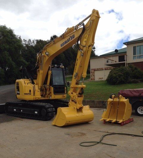 Yellow Excavator Parked on a Grassy Lot — A & S Cuthel Earthmoving & Transport in Coffs Harbour, NSW