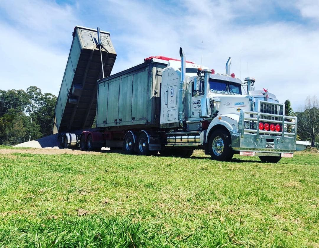 Large Blue Dump Truck Unloading a Raised Trailer on A Grassy Field — A & S Cuthel Earthmoving & Transport in Armidale, NSW