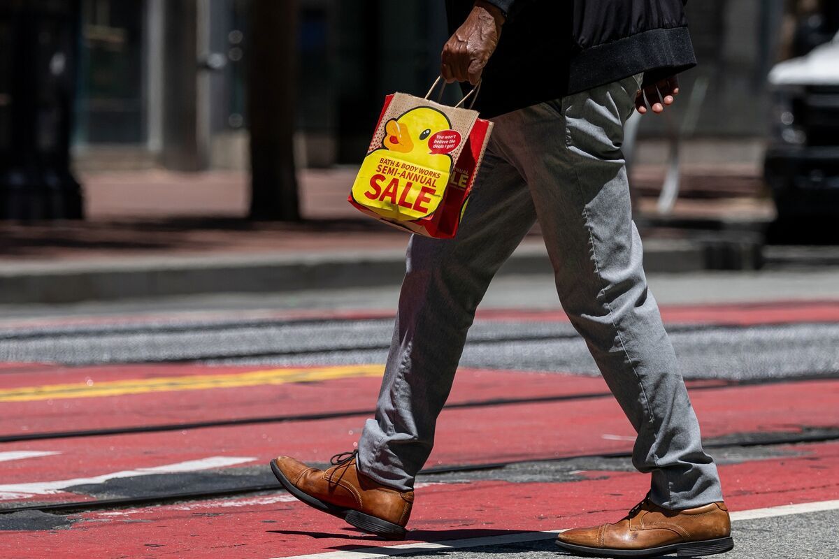 A person in gray trousers and brown shoes walks across a red crosswalk, carrying a small paper bag with a yellow duck.