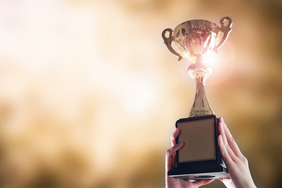 Hands hold up a golden trophy against a blurred, warm, glowing background.