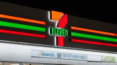 An illuminated 7-Eleven store sign at night, featuring the signature orange, green, and red stripes.