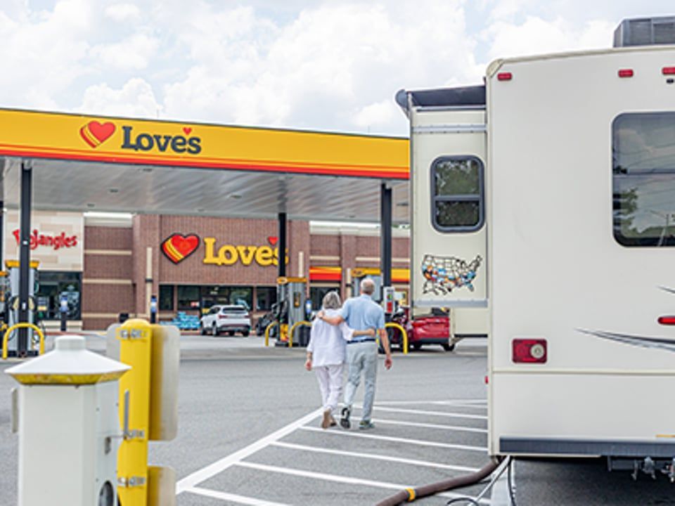 A couple walks hand-in-hand toward a Love's Travel Stop with an RV parked nearby.