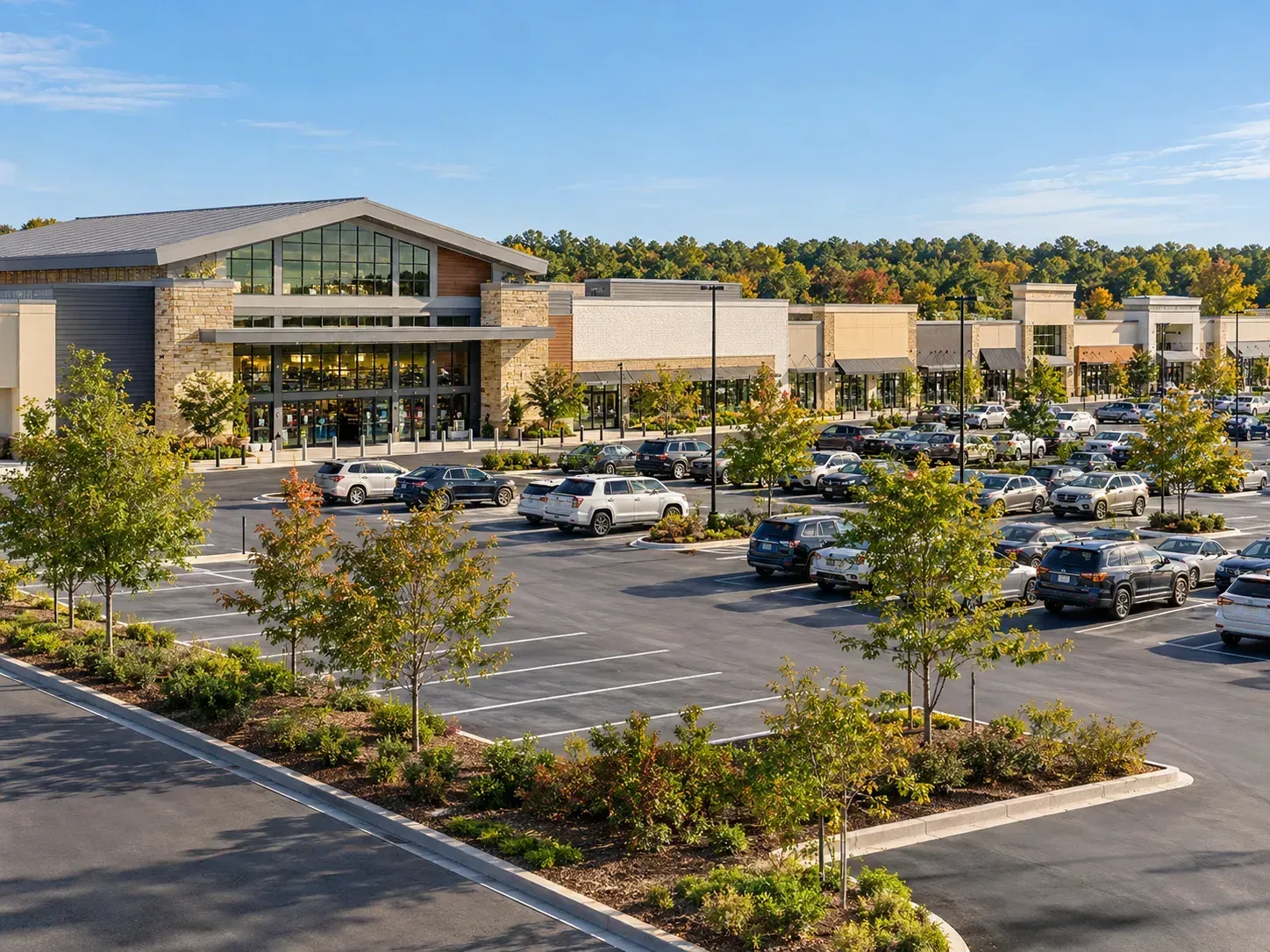 An elevated outdoor view of a modern shopping mall promenade with manicured greenery, palm trees, and pedestrians.