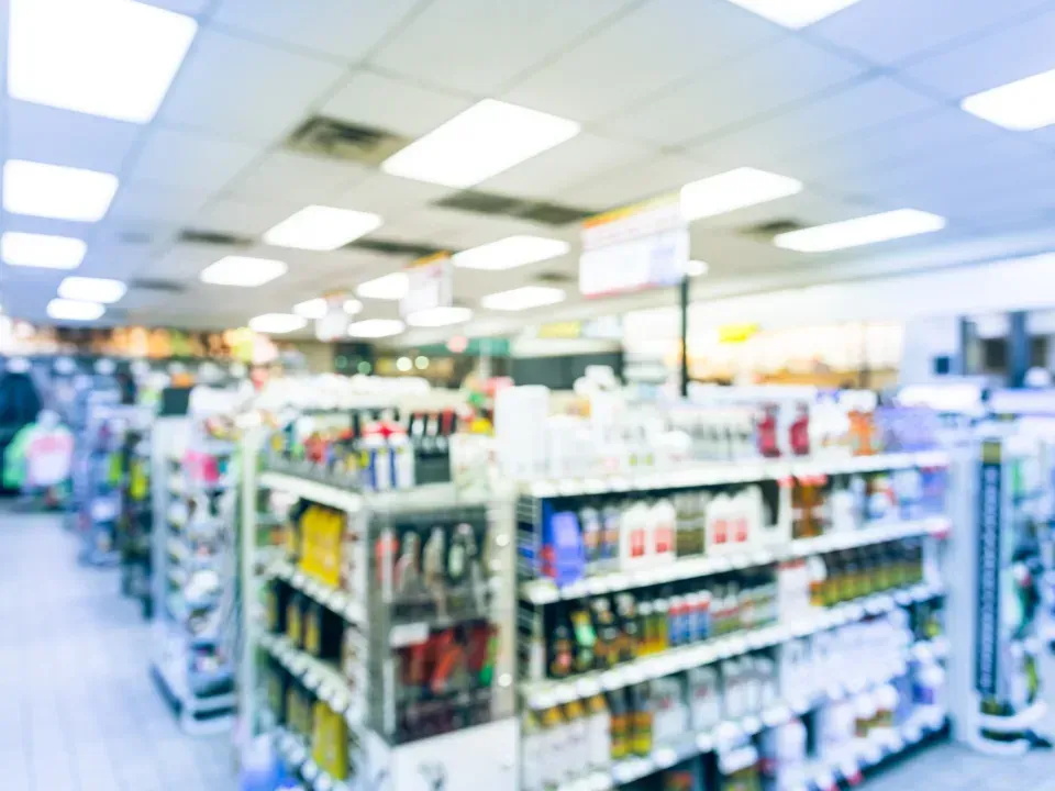 A blurred view down the aisle of a brightly lit convenience store, filled with shelves stocked with various products.