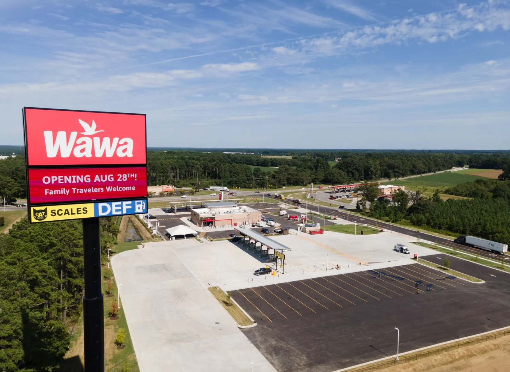 An aerial view of a new Wawa gas station and convenience store under a clear blue sky, featuring a prominent road sign.