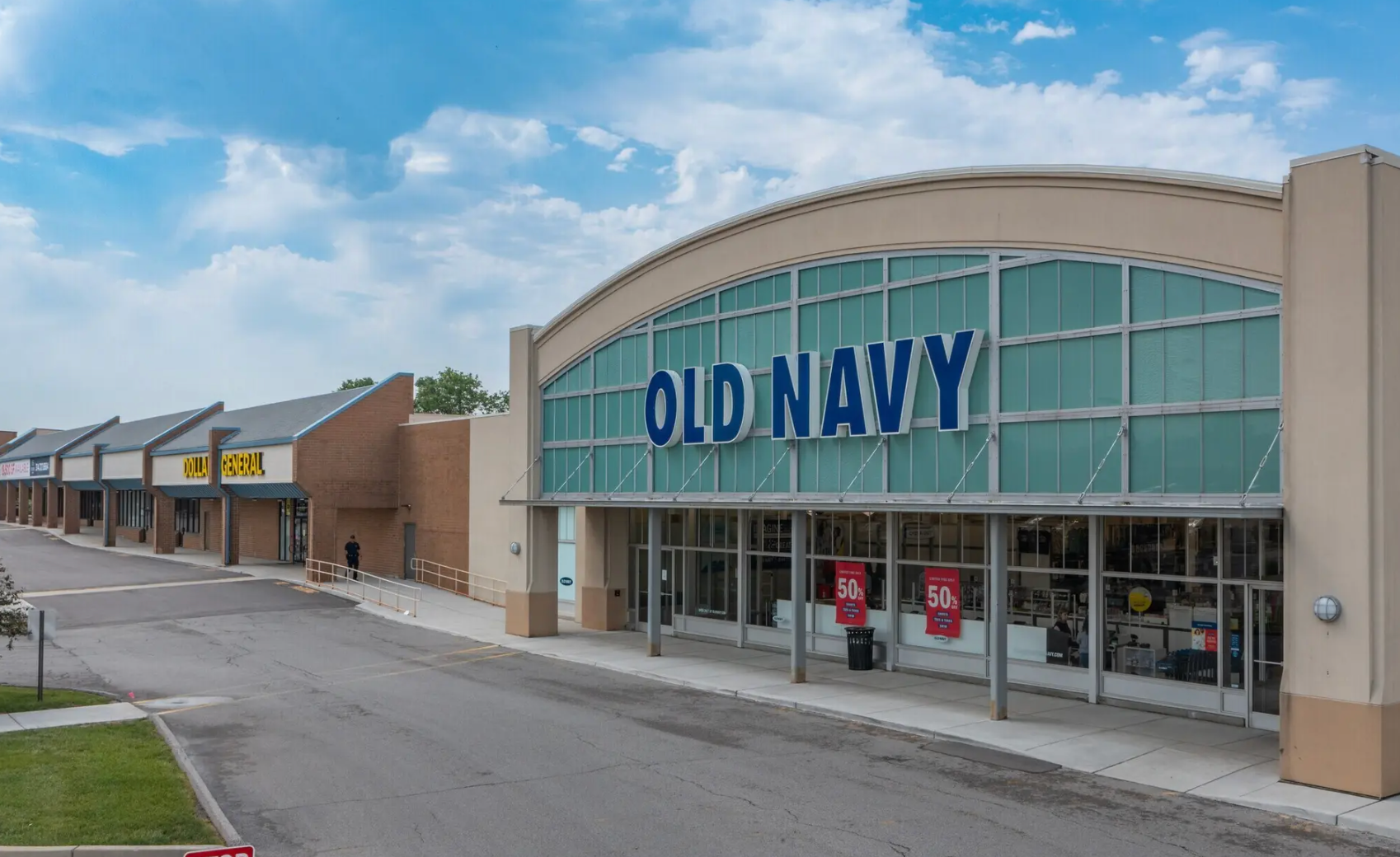 An Old Navy store storefront with a blue sign and glass windows in a strip mall under a blue sky.