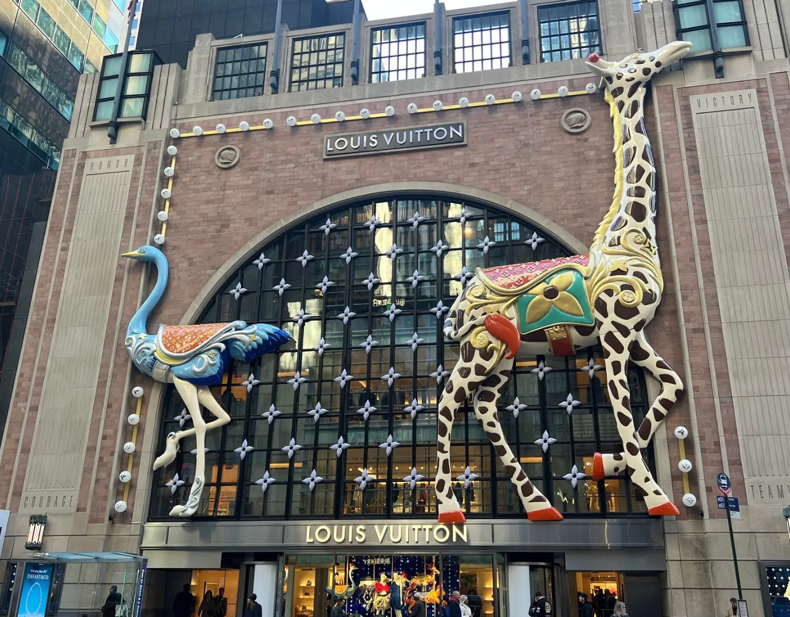A Louis Vuitton store front featuring large, decorative ostrich and giraffe sculptures flanking a glass arched window.