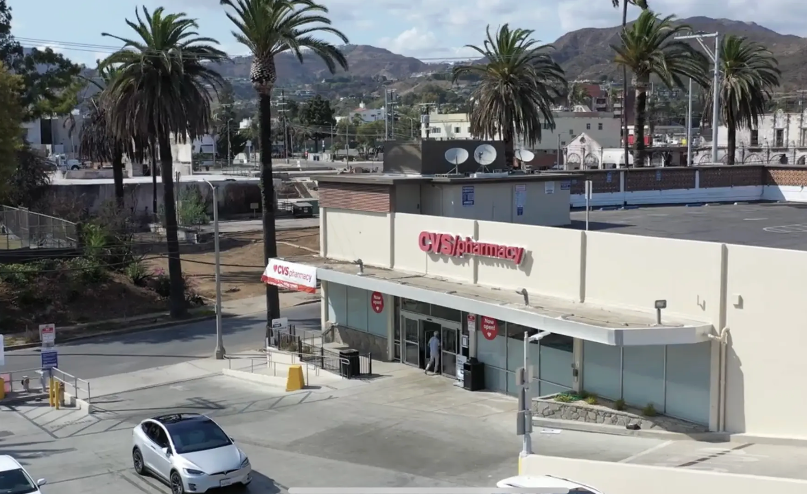 A CVS Pharmacy store exterior with a parking lot in front, framed by palm trees against a mountain backdrop.