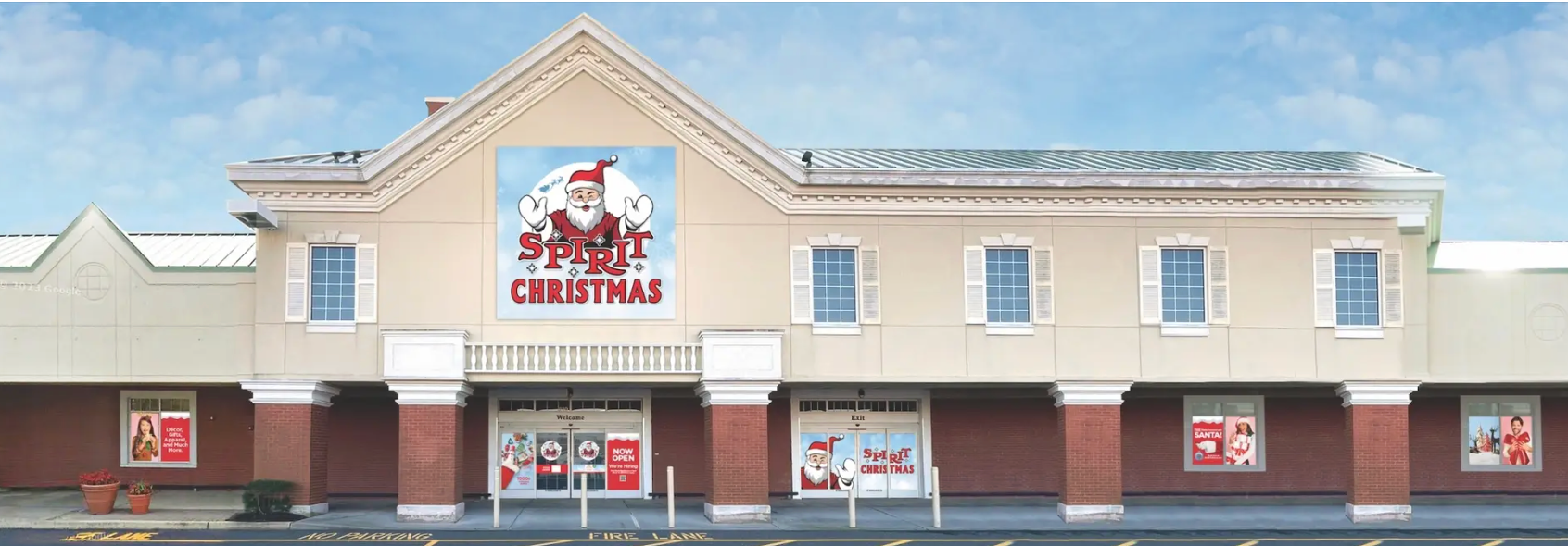 A Spirit Christmas store exterior with a large Santa logo on the tan building facade above brick-based store windows.