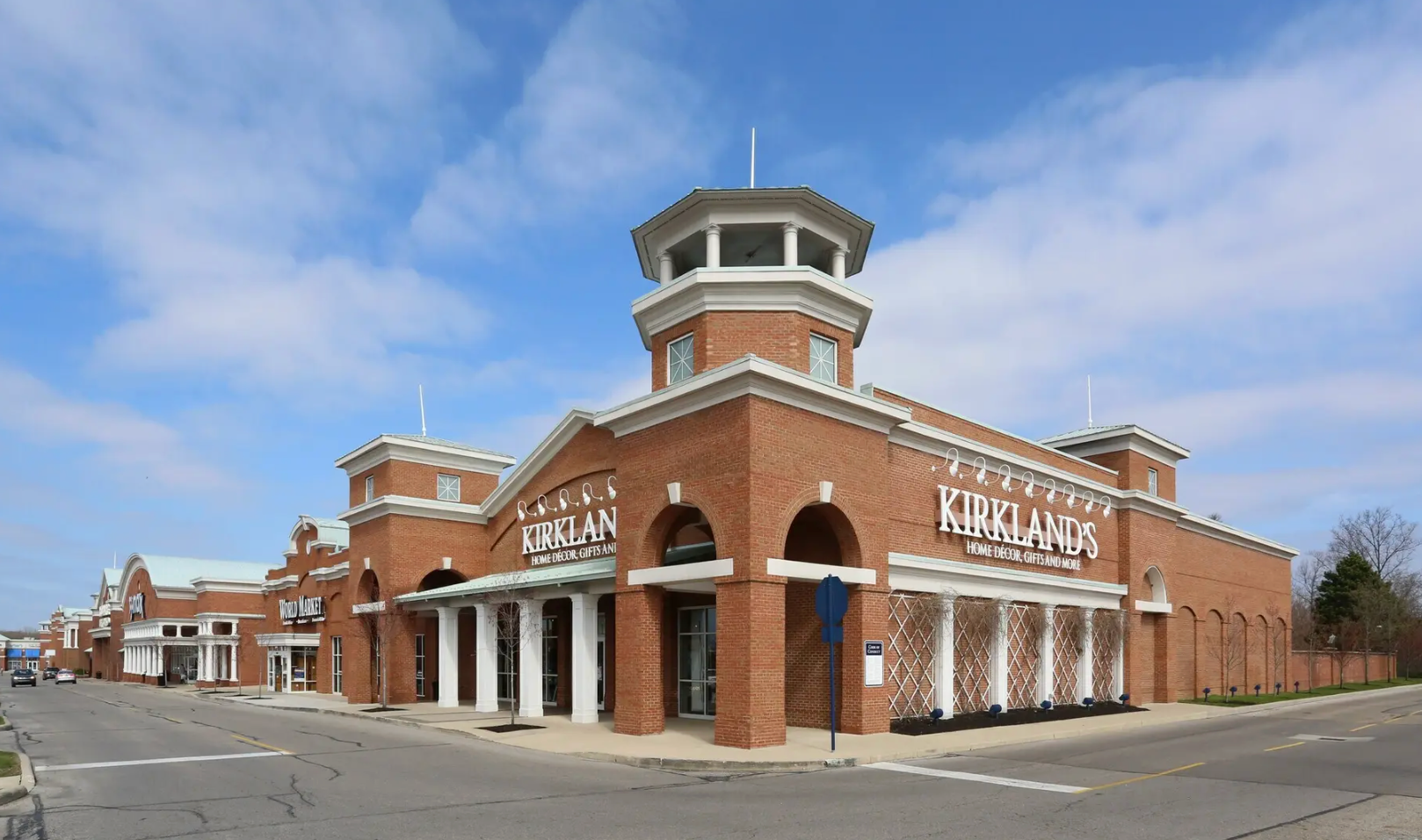 A brick shopping center featuring a prominent cupola tower against a blue sky, with 