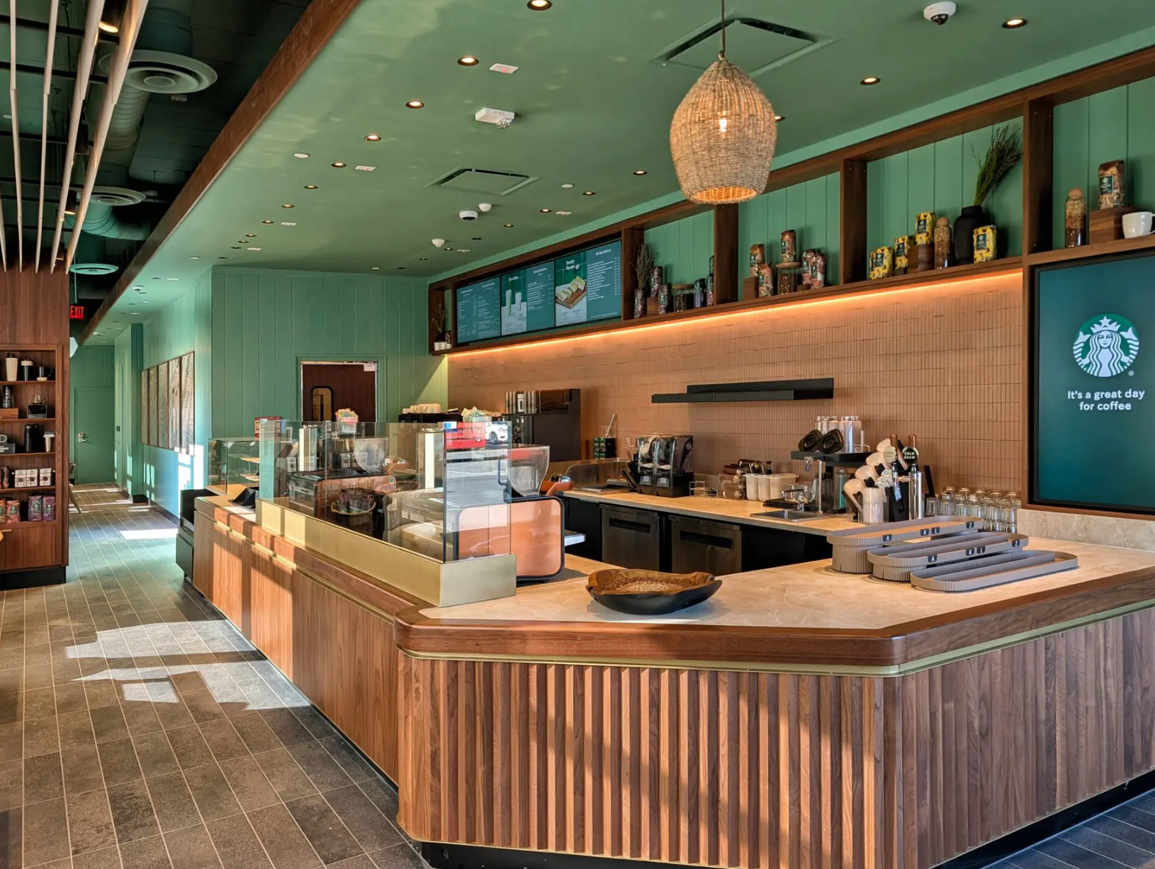 A modern Starbucks interior featuring a light green ceiling, warm wood paneling, and a large service counter.