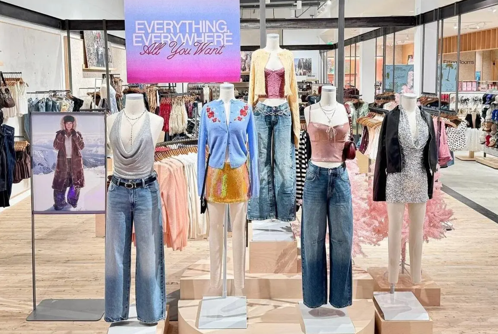 A clothing store display features mannequins in trendy outfits under a pink-to-blue gradient sign that says 