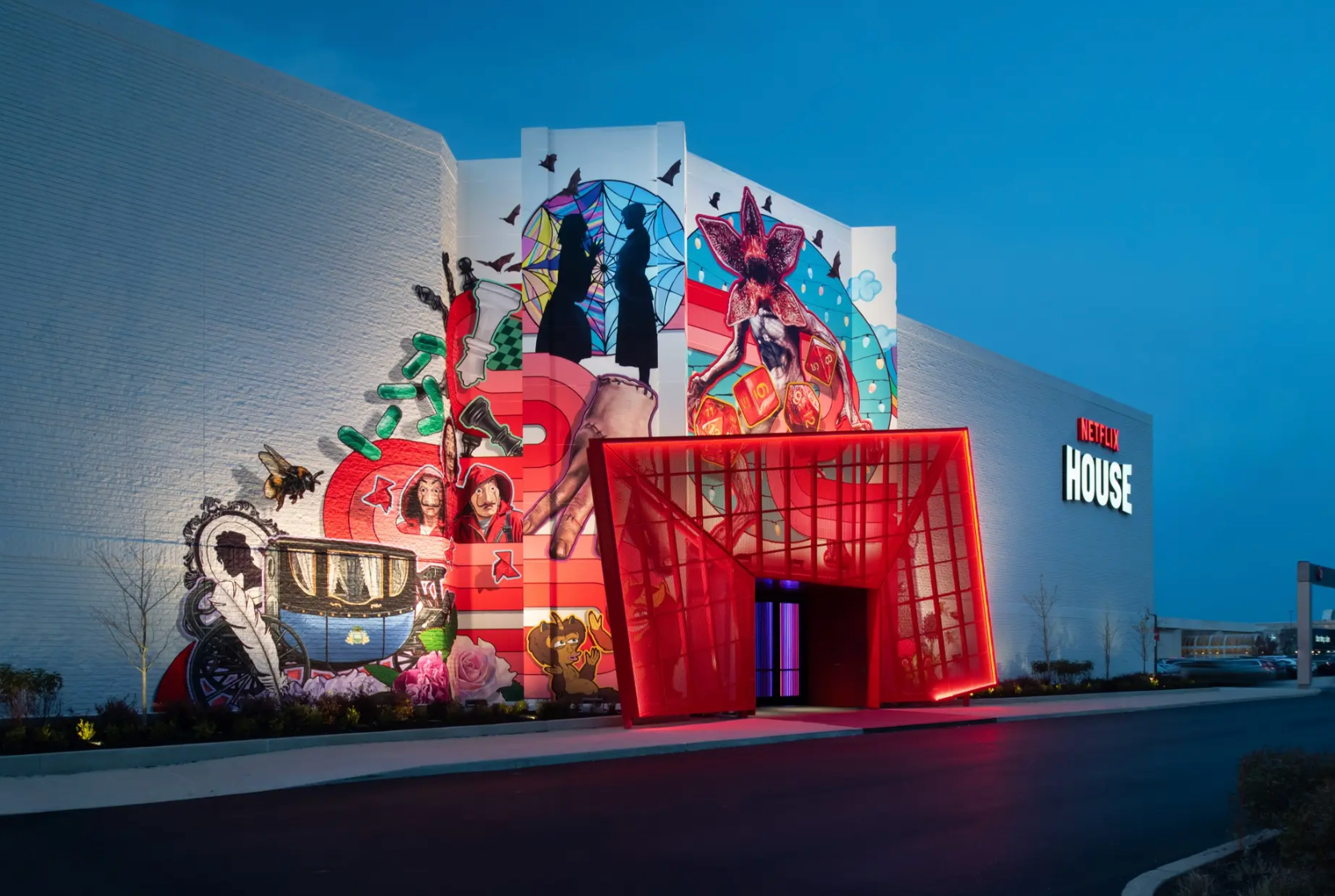 A building entrance with a large red structural gate and a colorful, intricate mural featuring silhouettes and icons.