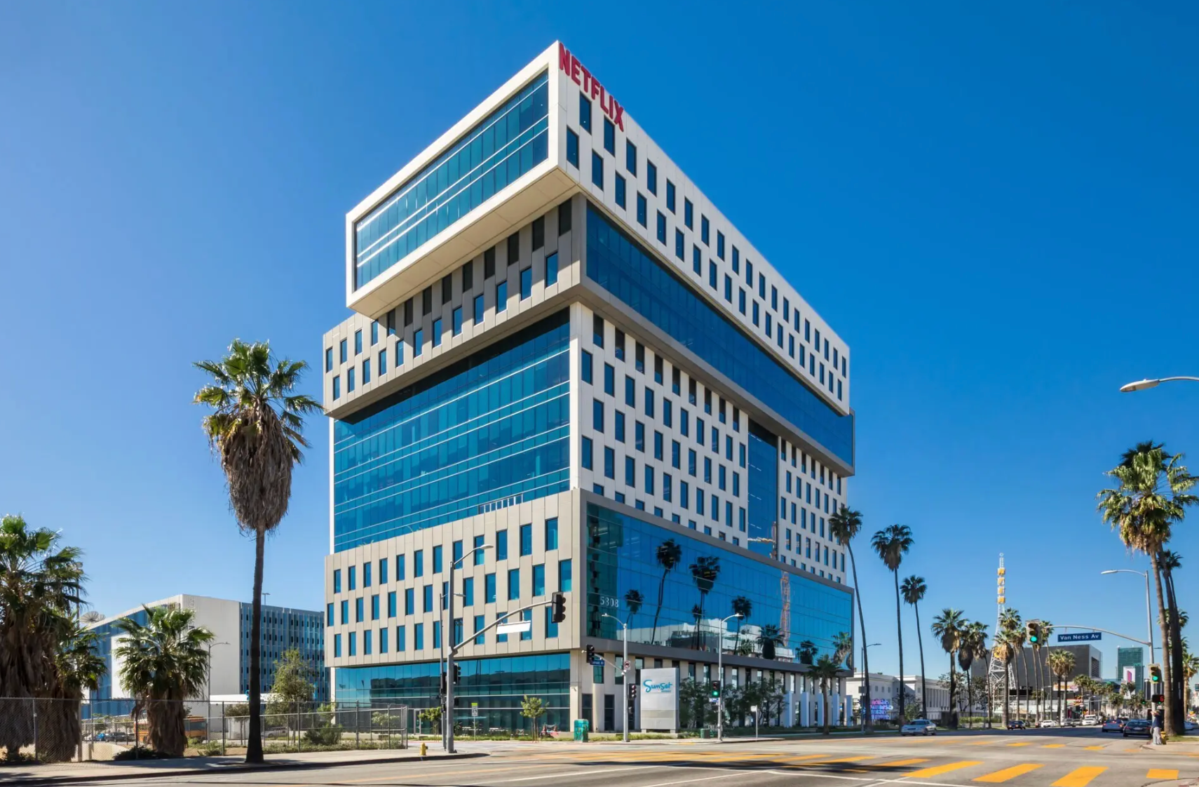 Modern multi-story office building with a glass and white facade under a clear blue sky, featuring the Netflix logo.