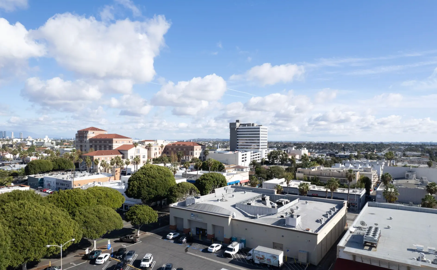 A sunny, elevated view of an urban area with a mix of low-rise commercial buildings, a tall gray tower, and trees.