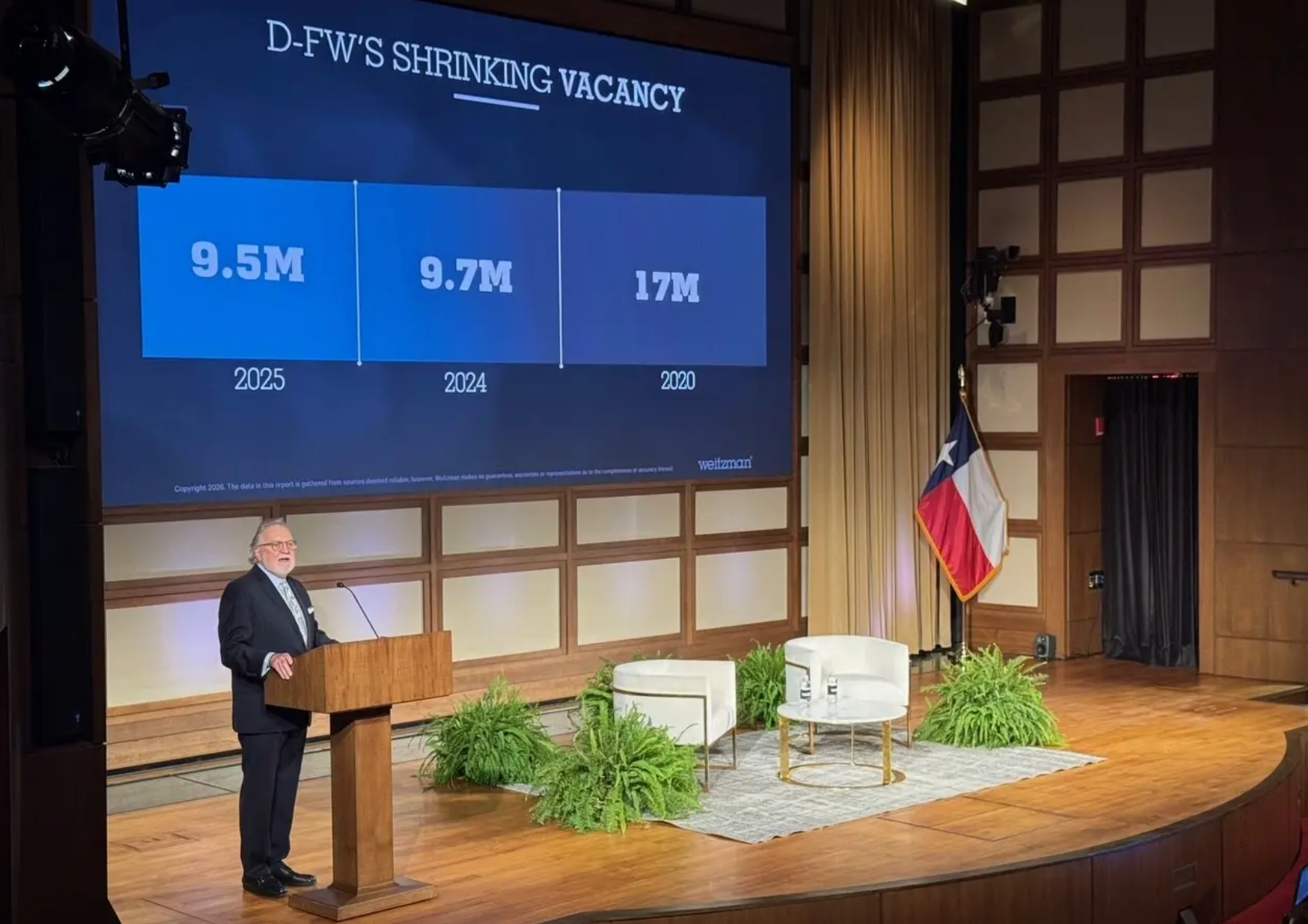 A speaker at a podium in front of a screen titled 