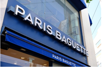 A low-angle view of a blue Paris Baguette storefront sign with white lettering.