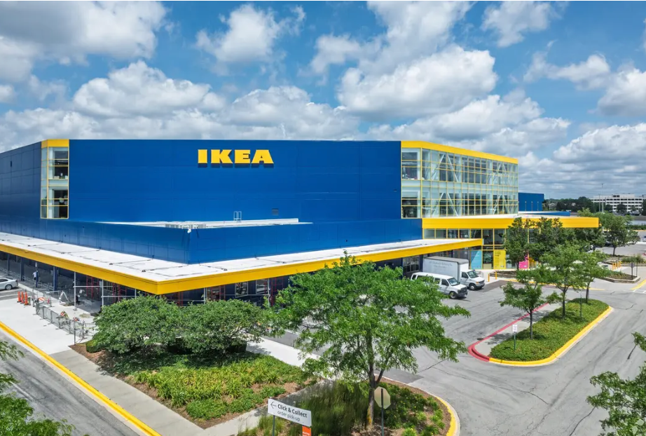 A wide-angle, exterior view of a large blue and yellow IKEA store under a blue sky with scattered clouds.