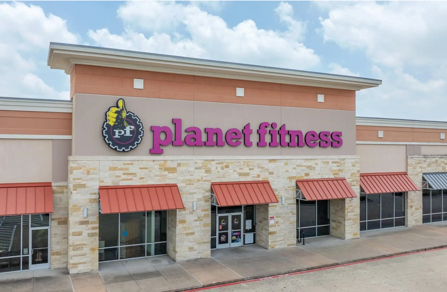 A Planet Fitness storefront in a strip mall with stone accents, purple signage, and reddish-brown metal awnings.