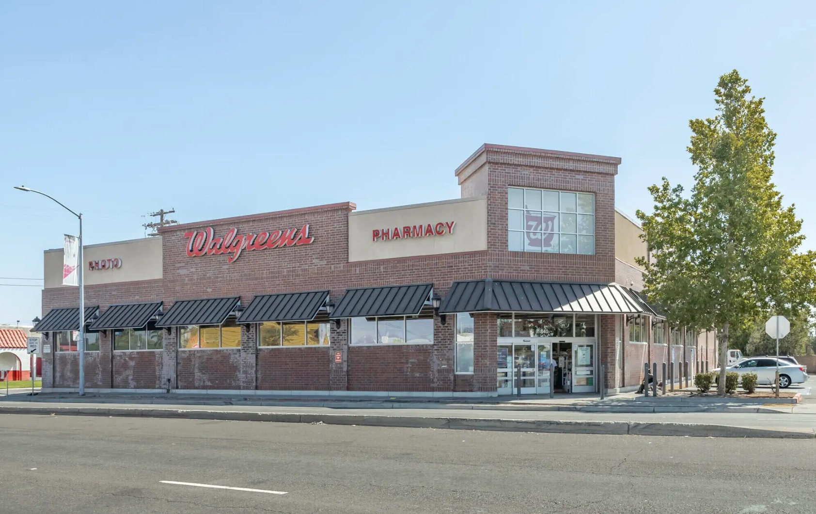 A brick Walgreens pharmacy building with a dark metal awning and a corner entrance on a sunny day.