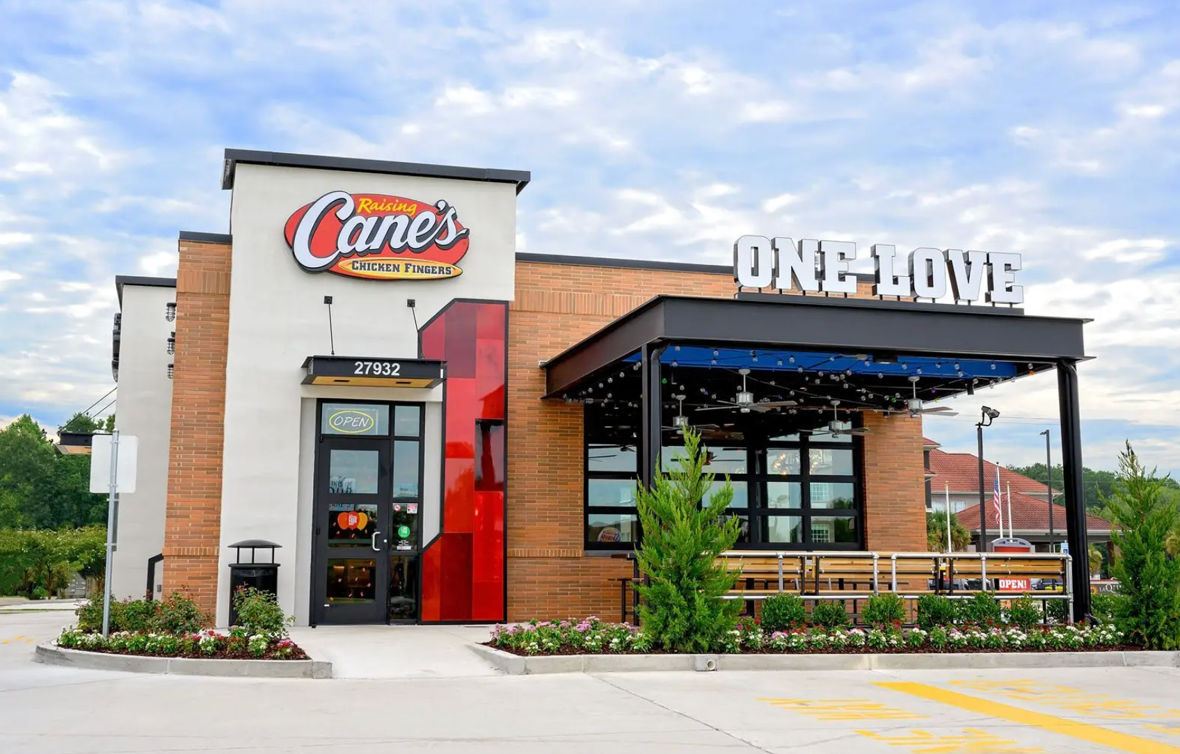 Modern Raising Cane's restaurant building with a wood-accented exterior, red vertical detail, and an outdoor patio area.
