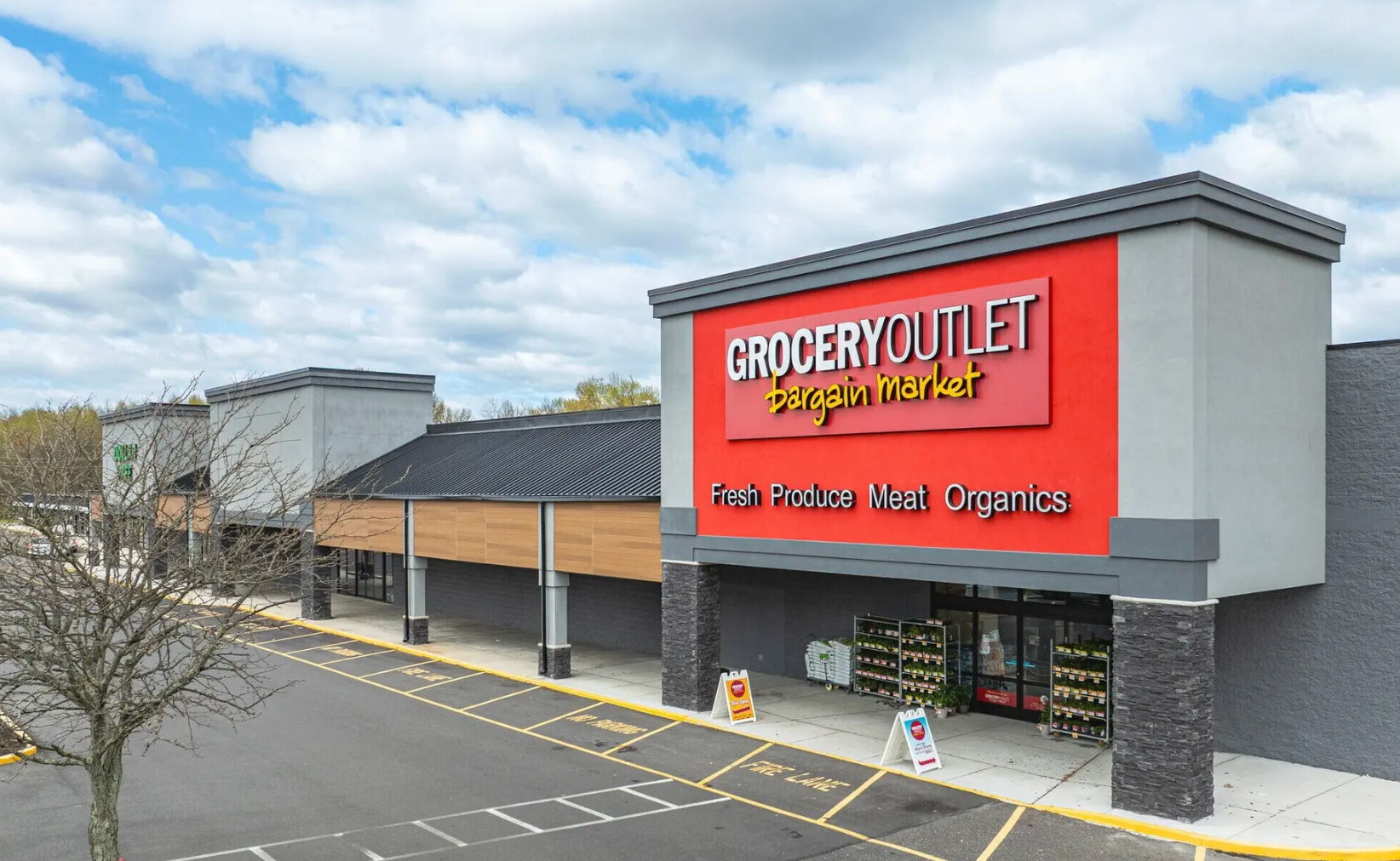 Grocery Outlet Bargain Market storefront in a strip mall with a large red sign and parking lot under a cloudy blue sky.