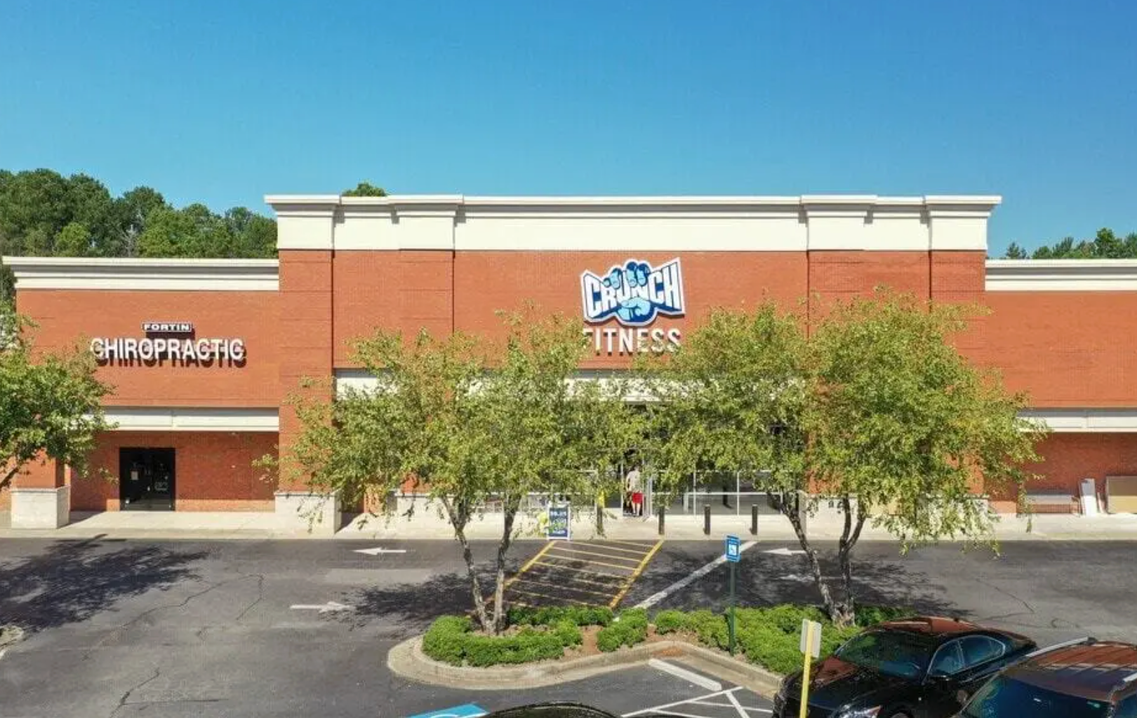 A brick strip mall featuring a Crunch Fitness gym and a chiropractic office under a clear blue sky.