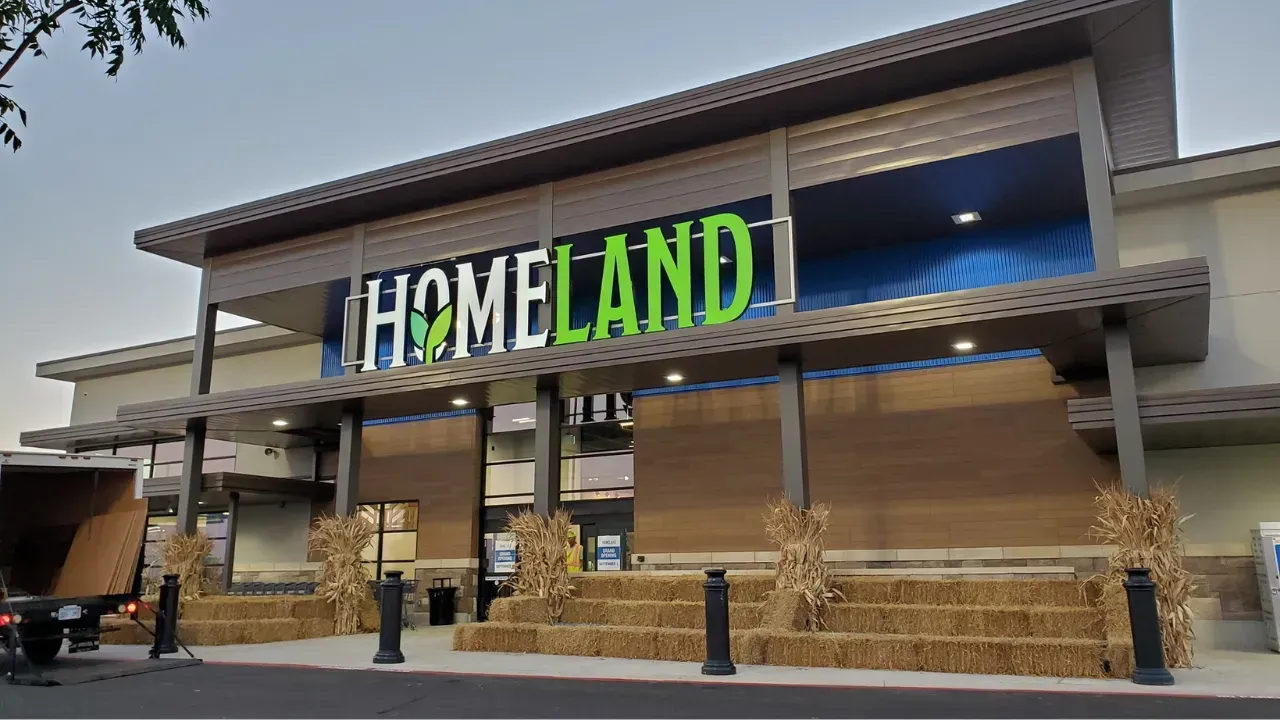 A Homeland grocery store entrance decorated with stacked hay bales and dried corn stalks under a modern canopy.