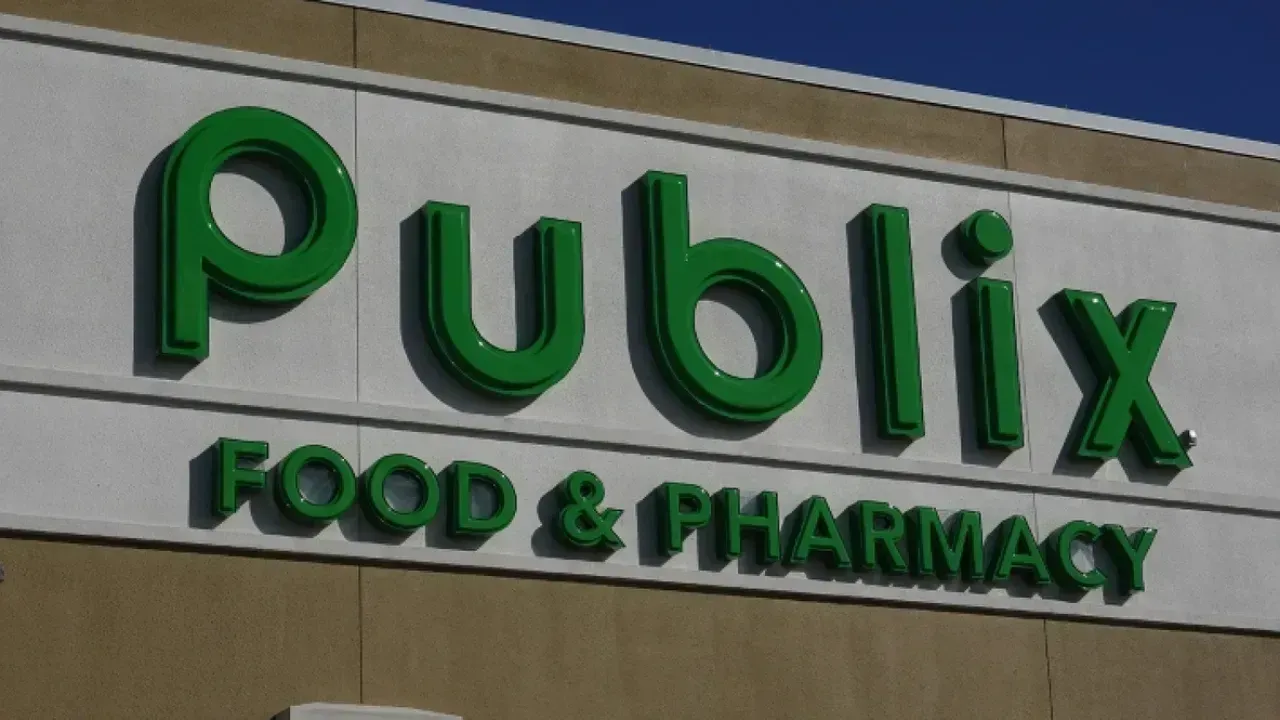 A green Publix Food & Pharmacy sign mounted on a white and beige building exterior against a blue sky.
