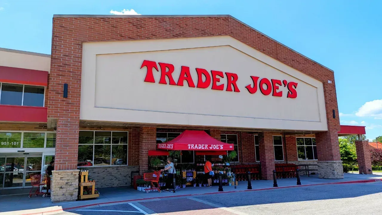 Exterior view of a brick Trader Joe's grocery store with a red promotional tent set up in front on a sunny day.