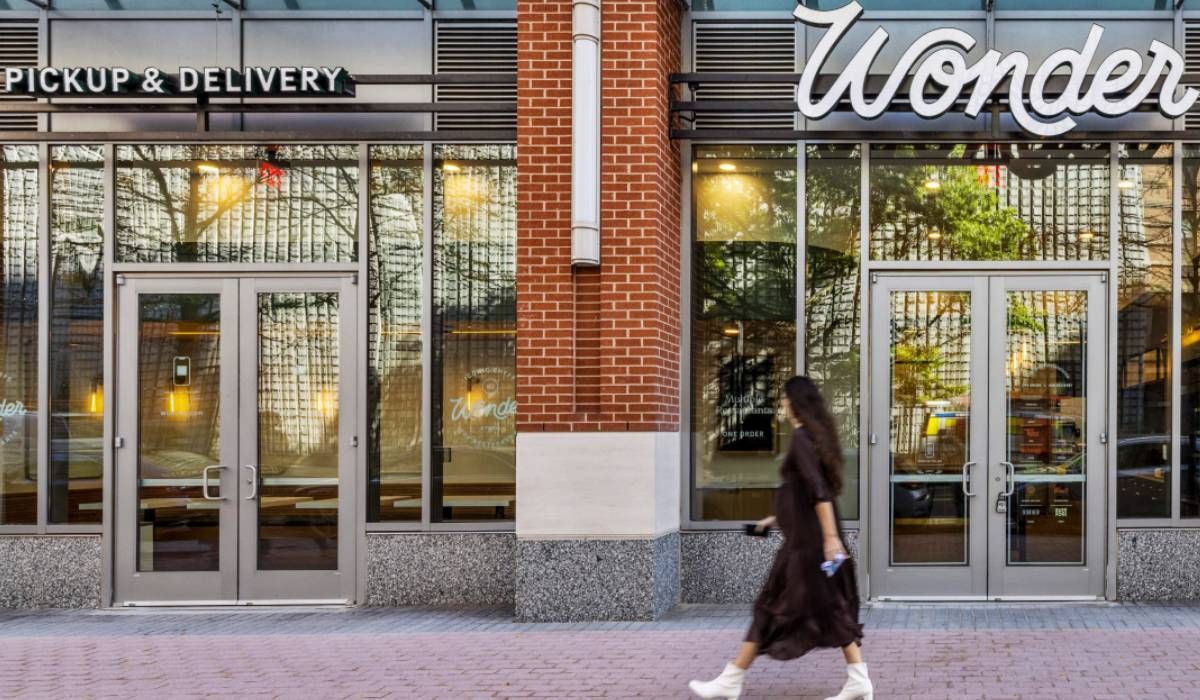 A person walks past the storefront of a Wonder restaurant with glass doors and a red brick column.