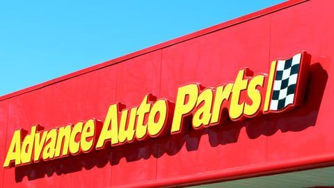 A red sign for Advance Auto Parts with yellow lettering and a checkered flag logo against a clear blue sky.