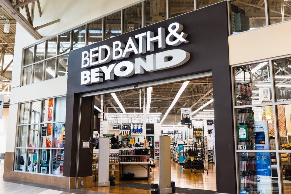 A storefront entrance for a Bed Bath & Beyond retail store with white branding on a black sign above the glass door.