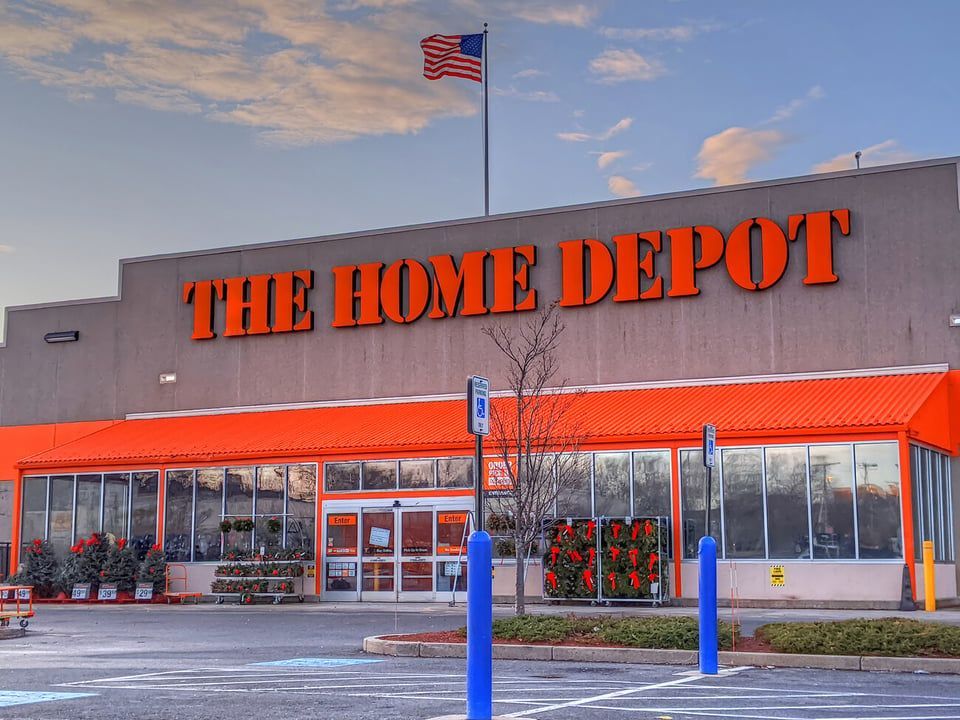 The exterior of a Home Depot store with its signature orange branding and an American flag flying on the roof.