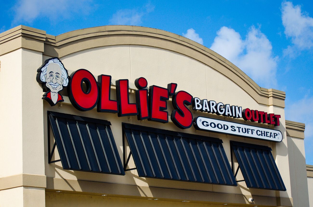 The exterior sign of an Ollie's Bargain Outlet store featuring its cartoon mascot logo against a bright blue sky.