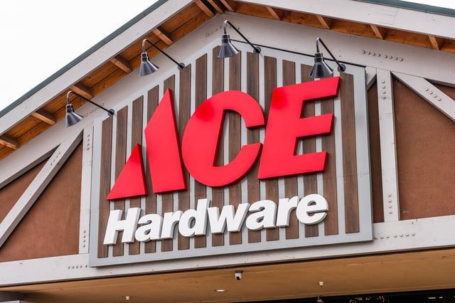 The Ace Hardware store logo sign with bold red lettering against a dark vertical wooden panel under a building overhang.