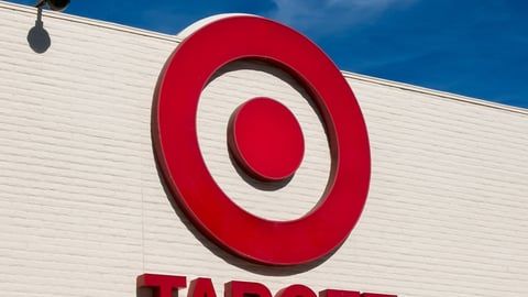 A red Target bullseye logo mounted on a light-colored brick exterior wall under a clear blue sky.
