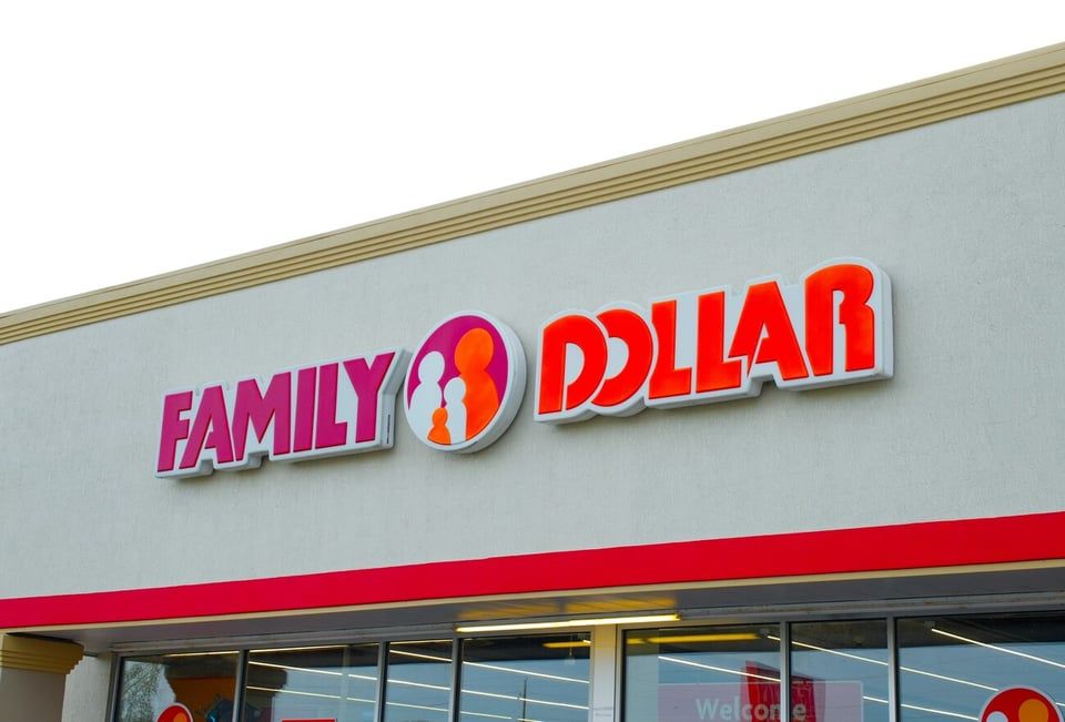 Exterior sign of a Family Dollar store featuring pink and red lettering and a circular logo on a gray building facade.