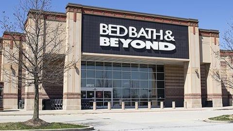 A Bed Bath & Beyond retail store with a black sign on a tan concrete building under a clear blue sky.