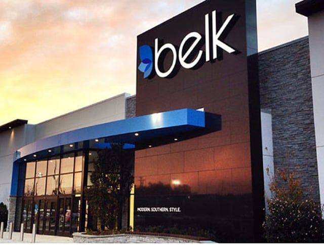 The exterior entrance of a Belk department store at sunset with a blue curved canopy and modern stone facade.