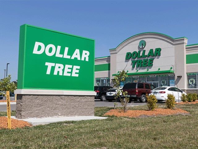 A Dollar Tree store exterior with a large green sign in the foreground under a clear blue sky.